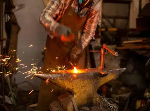 The blacksmith manually forging the molten metal on the anvil in smithy with spark fireworks Blacksmith's workshop