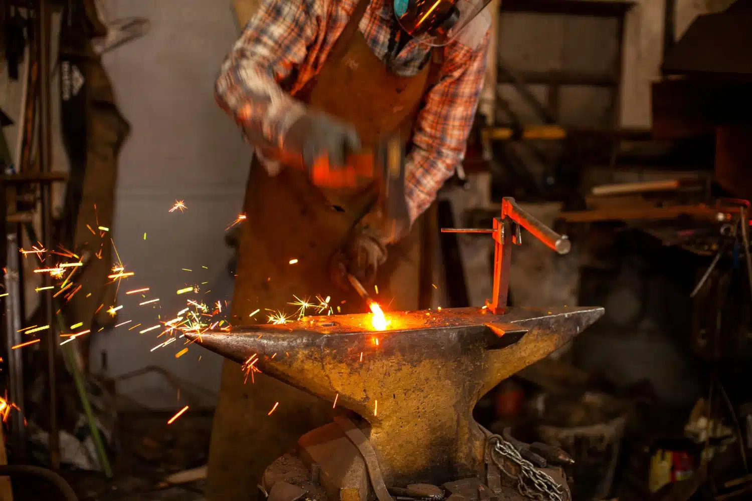 iron-mak The blacksmith manually forging the molten metal on the anvil in smithy with spark fireworks Blacksmith's workshop