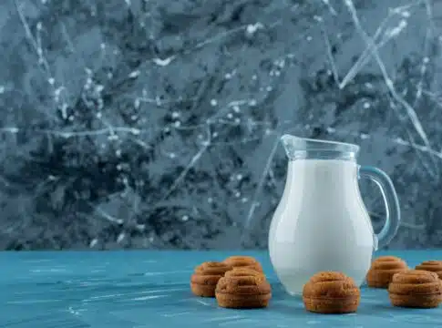 A glass pitcher of fresh milk with sweet round cookies