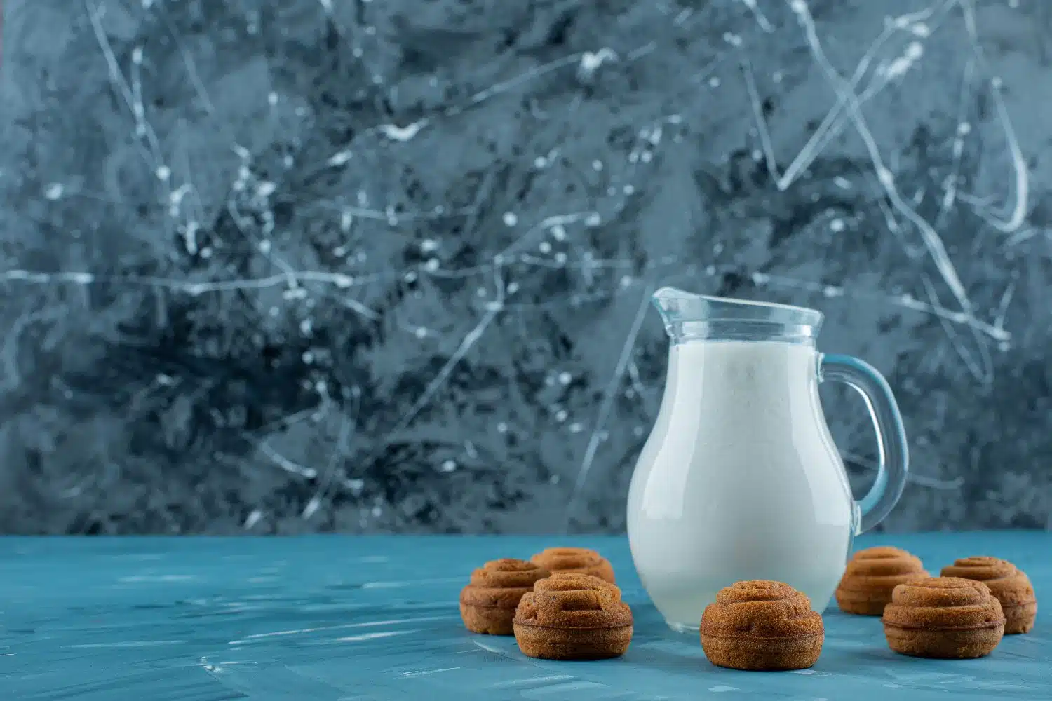 A glass pitcher of fresh milk with sweet round cookies